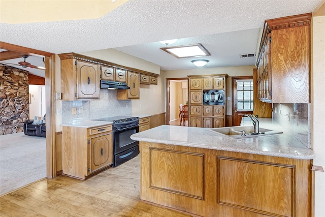 kitchen featuring light countertops, a sink, a peninsula, under cabinet range hood, and black appliances