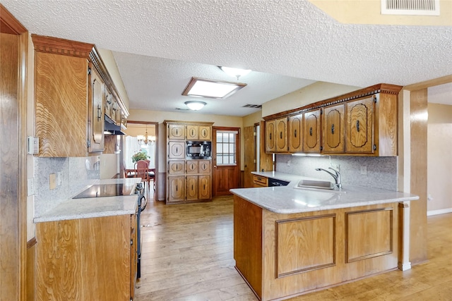 kitchen with black microwave, sink, stove, light hardwood / wood-style floors, and kitchen peninsula