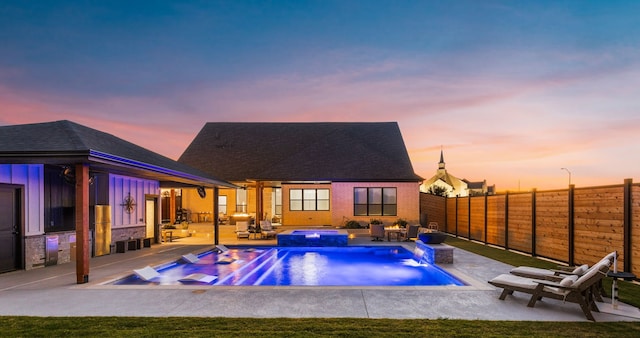 pool at dusk featuring an in ground hot tub, pool water feature, and a patio