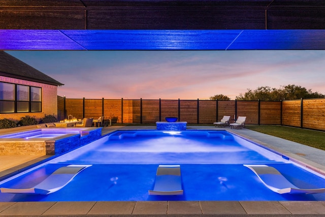 pool at dusk featuring an in ground hot tub and a patio