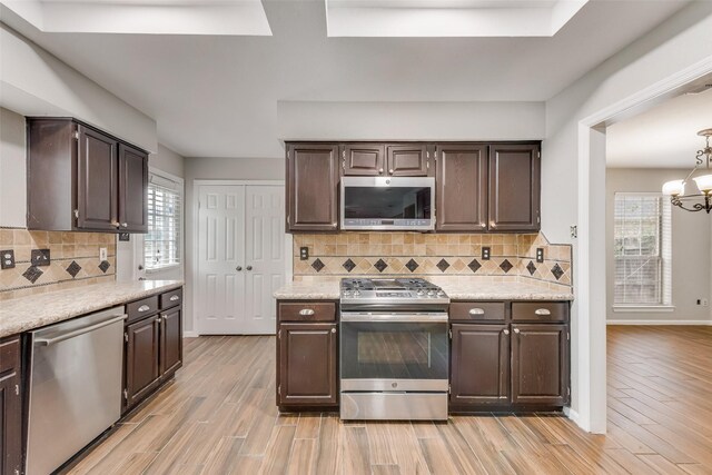 kitchen with appliances with stainless steel finishes, backsplash, an inviting chandelier, and light hardwood / wood-style flooring