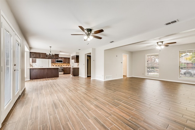 unfurnished living room featuring ceiling fan with notable chandelier and light hardwood / wood-style floors