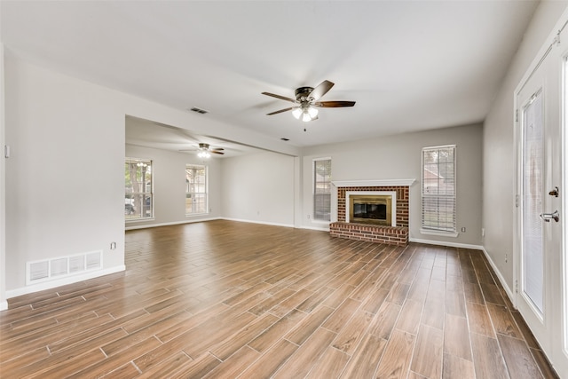 unfurnished living room with a healthy amount of sunlight, ceiling fan, wood-type flooring, and a brick fireplace