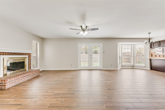 unfurnished living room with ceiling fan with notable chandelier, light hardwood / wood-style floors, french doors, and a brick fireplace