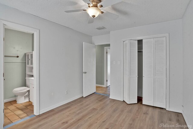 unfurnished bedroom featuring a closet, ensuite bath, light hardwood / wood-style flooring, and a textured ceiling