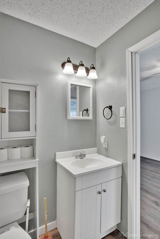 bathroom with hardwood / wood-style flooring, vanity, toilet, and a textured ceiling