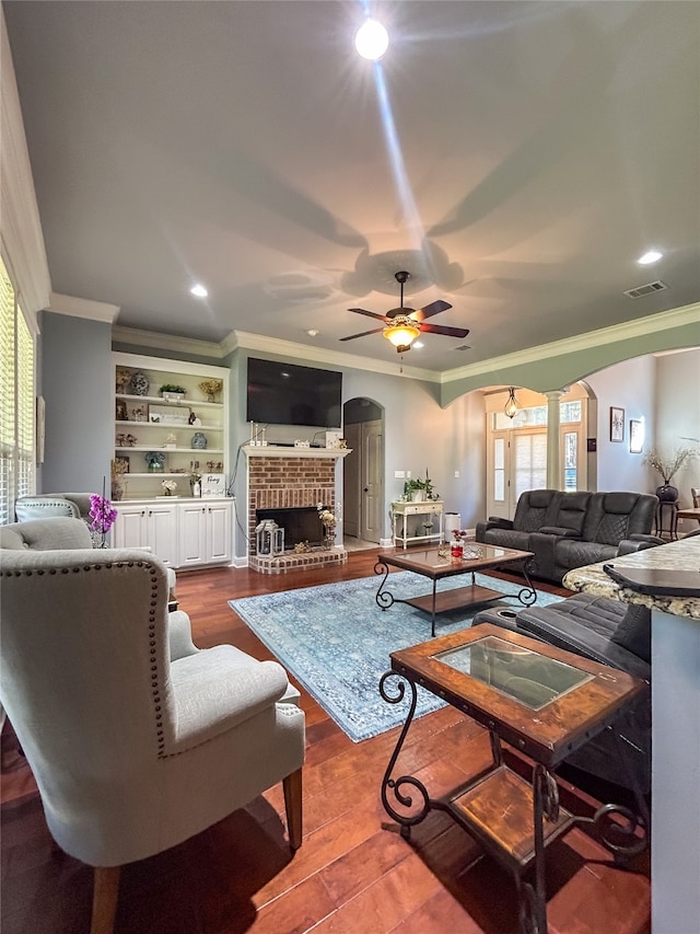 living room with hardwood / wood-style floors, crown molding, a brick fireplace, ceiling fan, and decorative columns