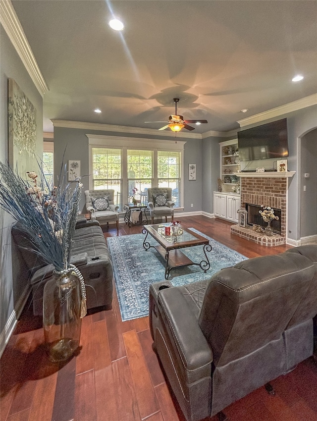 living room featuring ceiling fan, ornamental molding, dark wood-type flooring, and a brick fireplace