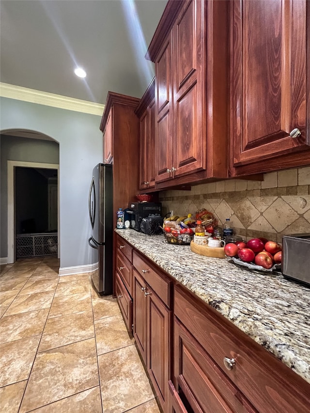 kitchen with stainless steel fridge, tasteful backsplash, light stone counters, and crown molding