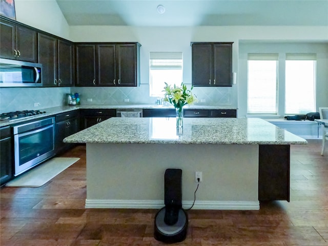 kitchen featuring light stone countertops, stainless steel appliances, a kitchen island, and a healthy amount of sunlight