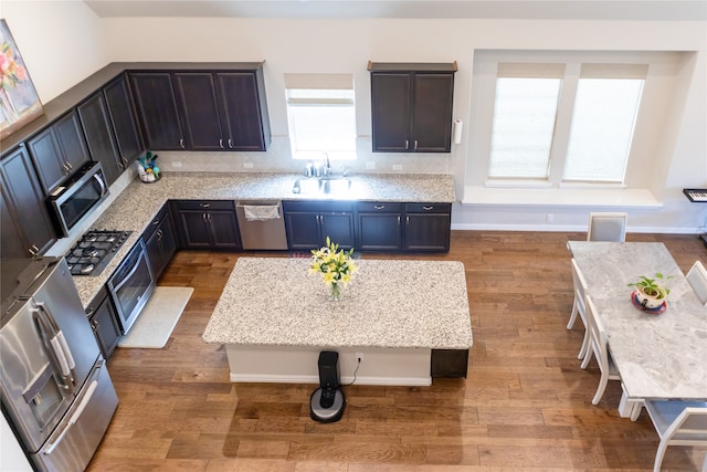 kitchen featuring a kitchen breakfast bar, light stone countertops, wood-type flooring, and appliances with stainless steel finishes