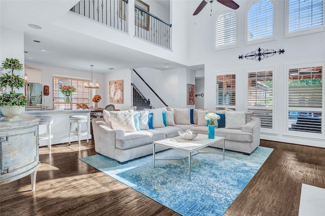 living room with dark hardwood / wood-style flooring, a towering ceiling, and ceiling fan with notable chandelier