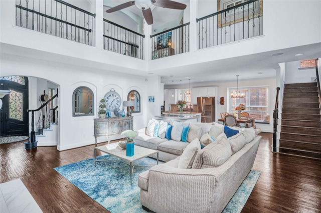 living room with ceiling fan with notable chandelier, dark hardwood / wood-style flooring, and a towering ceiling