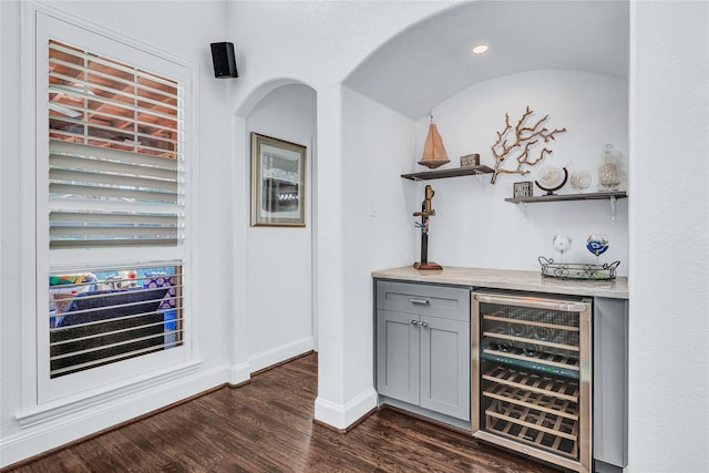 bar with dark wood-type flooring, wine cooler, and gray cabinetry