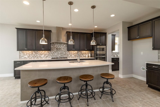 kitchen featuring appliances with stainless steel finishes, an island with sink, hanging light fixtures, and wall chimney range hood