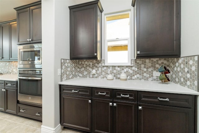 kitchen featuring decorative backsplash, dark brown cabinetry, stainless steel microwave, and light tile patterned flooring