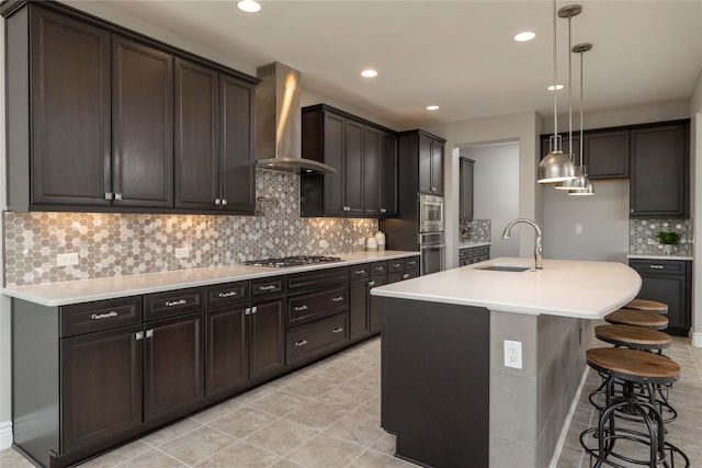 kitchen featuring sink, a kitchen island with sink, hanging light fixtures, wall chimney range hood, and decorative backsplash