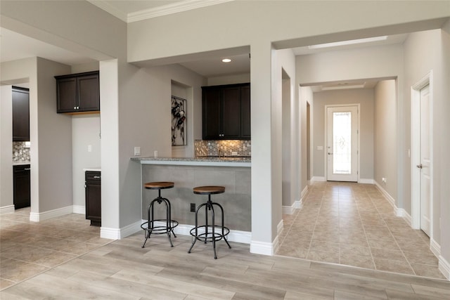 kitchen with light stone countertops, kitchen peninsula, crown molding, light hardwood / wood-style floors, and dark brown cabinets