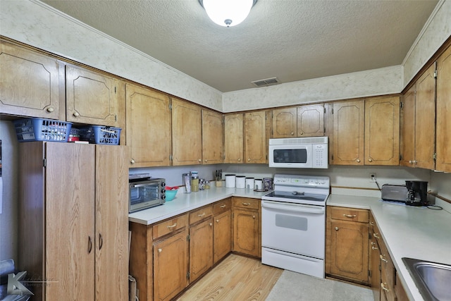 kitchen featuring sink, white appliances, a textured ceiling, and light wood-type flooring