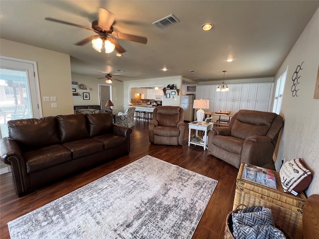 living room with ceiling fan with notable chandelier and dark wood-type flooring