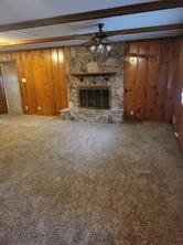 unfurnished living room with carpet, a stone fireplace, wood walls, and beamed ceiling