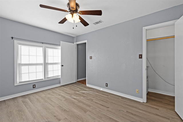 unfurnished bedroom featuring a walk in closet, a closet, ceiling fan, and light wood-type flooring