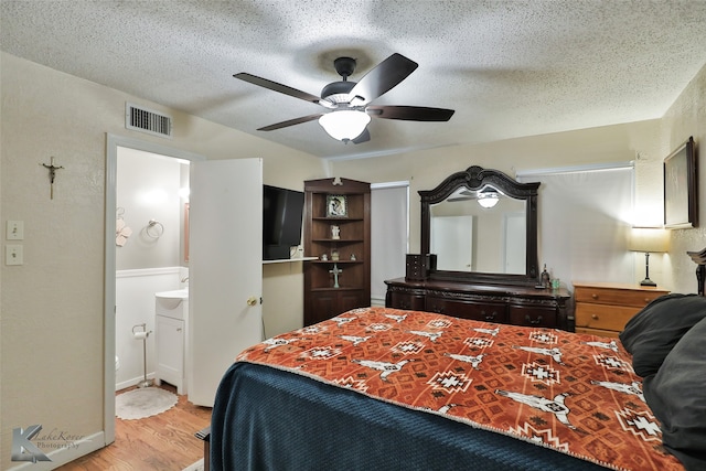 bedroom with a textured ceiling, ensuite bathroom, light hardwood / wood-style flooring, and ceiling fan