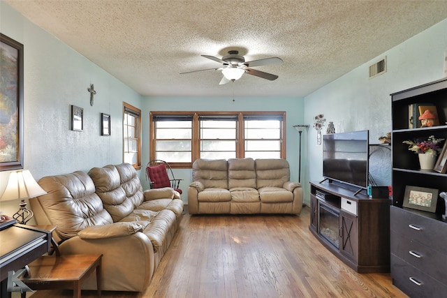 living room featuring ceiling fan, a textured ceiling, and light wood-type flooring