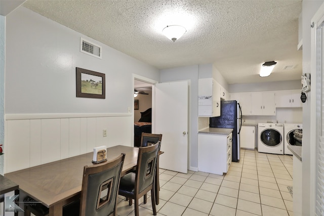 kitchen with white cabinets, black fridge, light tile patterned floors, a textured ceiling, and washing machine and clothes dryer