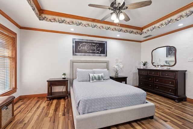 bedroom with hardwood / wood-style floors, ceiling fan, ornamental molding, and a tray ceiling