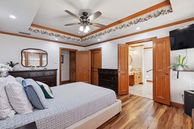 bedroom with ceiling fan, a raised ceiling, ensuite bathroom, hardwood / wood-style floors, and ornamental molding