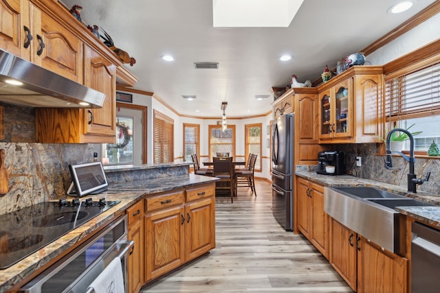 kitchen featuring sink, light hardwood / wood-style flooring, dark stone countertops, exhaust hood, and appliances with stainless steel finishes