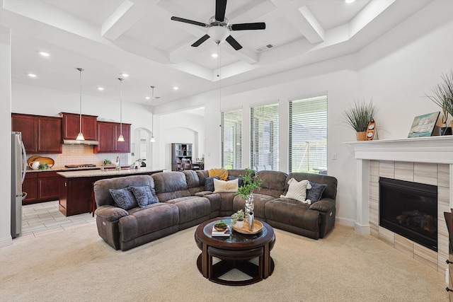 carpeted living room with beam ceiling, ceiling fan, sink, coffered ceiling, and a tiled fireplace