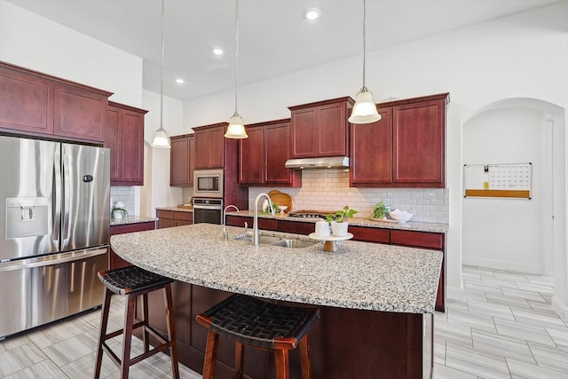 kitchen featuring appliances with stainless steel finishes, a breakfast bar, sink, a center island with sink, and decorative light fixtures