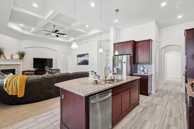 kitchen with a tile fireplace, hanging light fixtures, sink, an island with sink, and stainless steel appliances