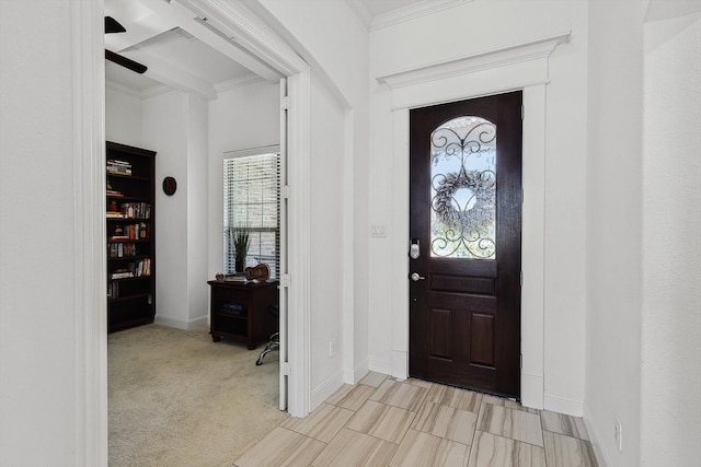 entryway featuring light carpet, beamed ceiling, ornamental molding, and ceiling fan