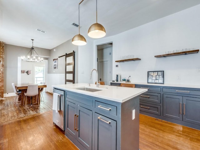 kitchen featuring a barn door, visible vents, a kitchen island with sink, light countertops, and a sink