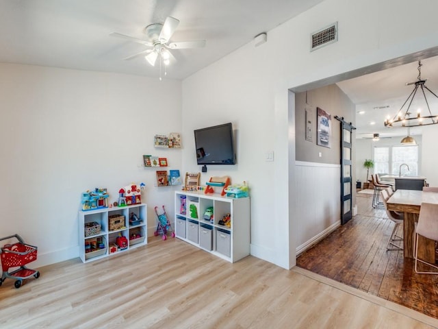 rec room featuring a barn door, ceiling fan with notable chandelier, and light hardwood / wood-style floors