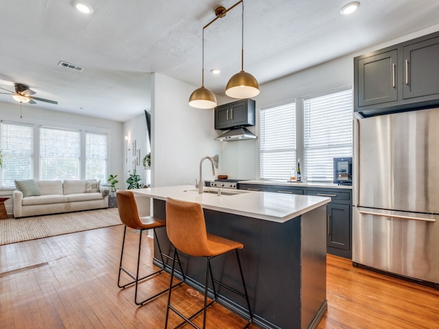 kitchen featuring sink, a kitchen breakfast bar, stainless steel fridge, a kitchen island with sink, and light wood-type flooring