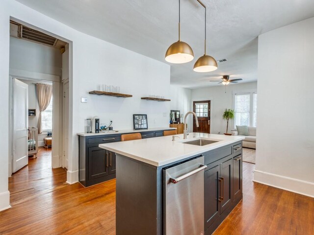 kitchen featuring a kitchen island with sink, sink, a barn door, decorative light fixtures, and light hardwood / wood-style floors