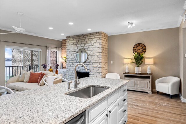 kitchen featuring light stone countertops, sink, ornamental molding, white cabinets, and light wood-type flooring