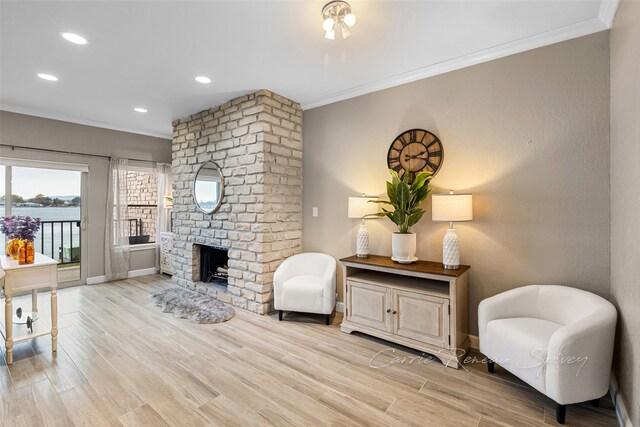 sitting room with light wood-type flooring, a brick fireplace, and crown molding