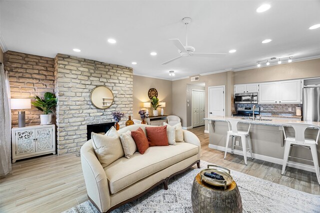 living room with crown molding, light hardwood / wood-style flooring, ceiling fan, and a brick fireplace