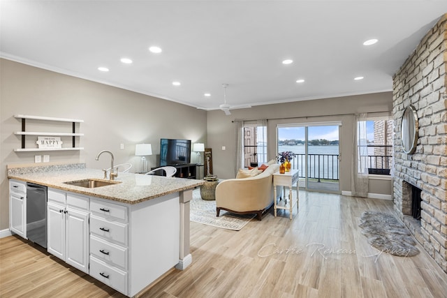 kitchen featuring sink, dishwasher, a brick fireplace, light stone counters, and white cabinets