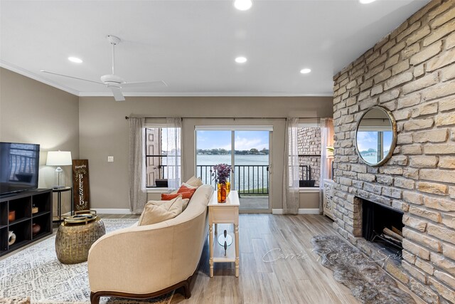 living room featuring ceiling fan, a brick fireplace, crown molding, a water view, and light wood-type flooring