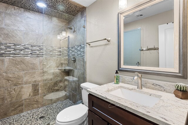 bathroom with vanity, toilet, and a tile shower