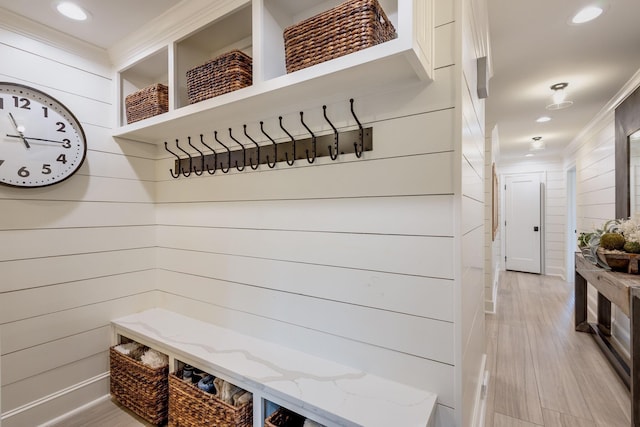 mudroom with crown molding, wooden walls, and light wood-type flooring