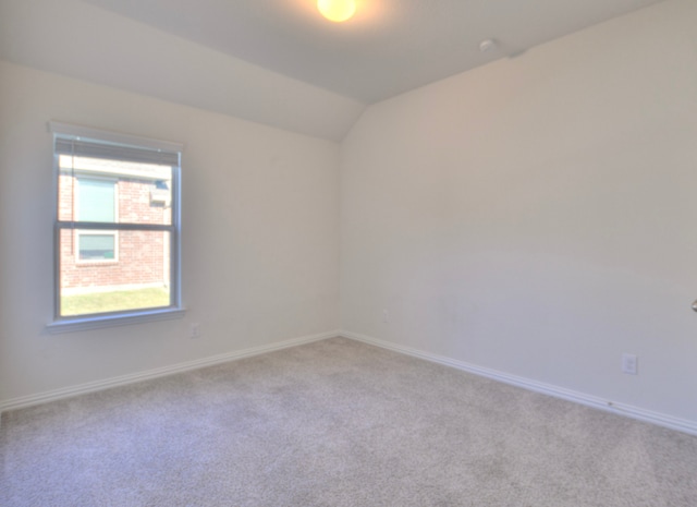 spare room featuring light colored carpet and lofted ceiling