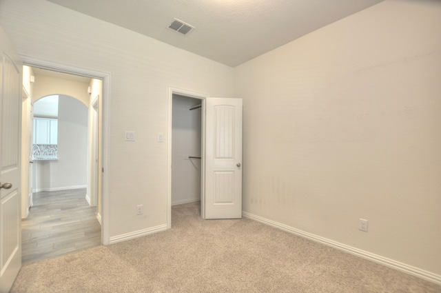 unfurnished bedroom with a walk in closet and light carpet