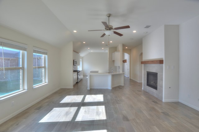 unfurnished living room featuring light wood-type flooring, ceiling fan, sink, a tile fireplace, and lofted ceiling